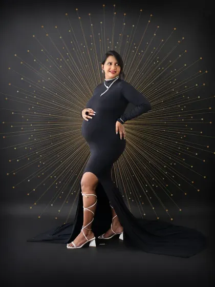 A powerful and stylish solo portrait. The mom-to-be strikes a confident pose in a sleek black gown against a dramatic, creative backdrop.