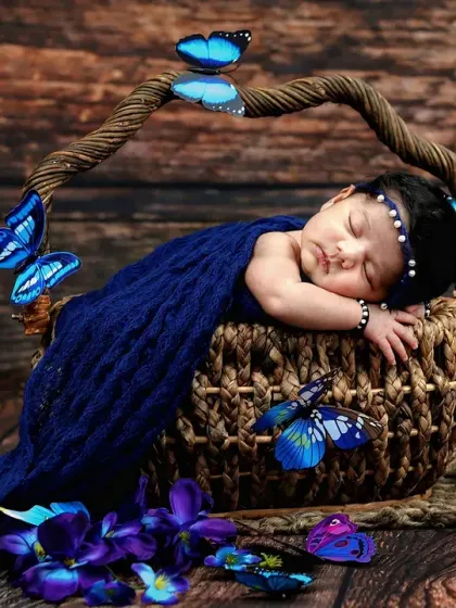Wrapped in a beautiful blue knit blanket, this newborn sleeps in a basket adorned with delicate blue butterflies.