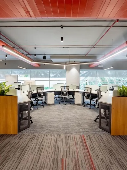 An industrial-inspired workspace featuring exposed red ductwork and a unique curved workstation layout. Planters are used as natural dividers, softening the industrial elements and adding a touch of green to the work floor.
