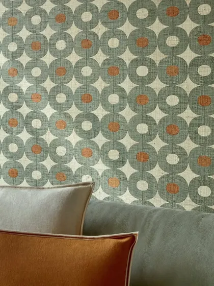 A bold, graphic wallpaper from Élitis, woven from raffia. The repeating circle pattern in a cool grey-green and rust orange adds a richly artisanal and contemporary feel to the wall.