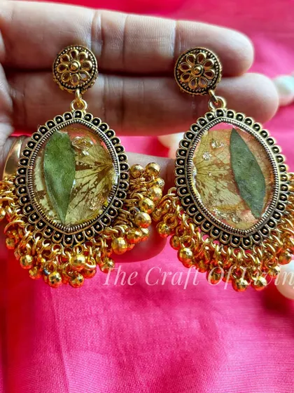 A pair of traditional gold-toned earrings with preserved green leaves inside. This shows how I can use different parts of a plant to create unique jewelry.