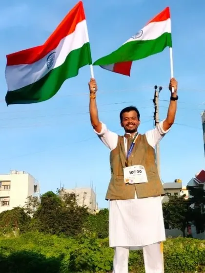 A triumphant runner holds two Indian flags high, celebrating his finish at the Freedom Run.