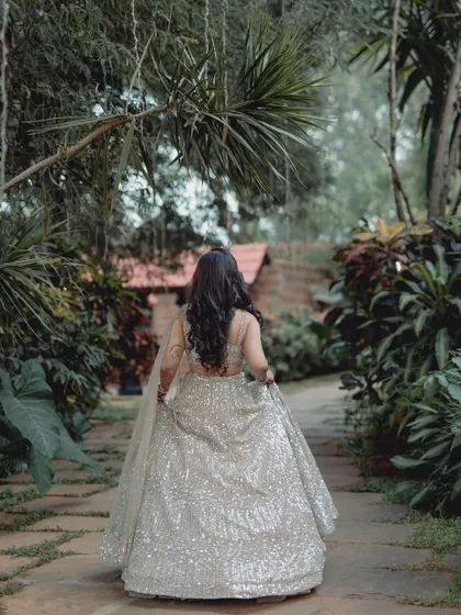 A shot from behind, capturing the bride as she walks through the garden path, showcasing the beautiful trail of her lehenga.