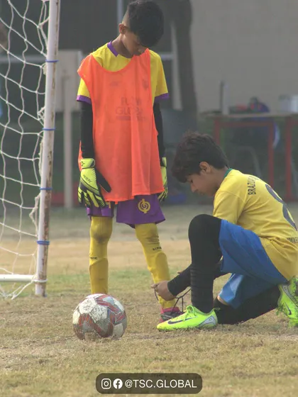 Teamwork is about helping each other succeed. Here, one player helps another tie his shoelaces before a big game, a simple act of camaraderie that defines our community.