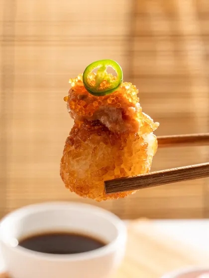 A single piece of crispy rice sushi held by chopsticks. This minimalist shot puts all the focus on the texture and toppings.