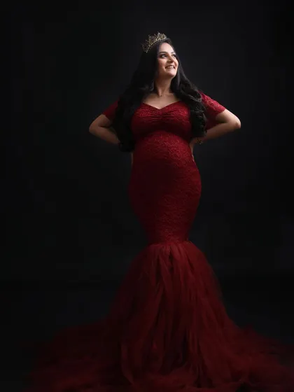 Looking up with hope and joy. This portrait captures the mom-to-be's radiant smile and regal presence in her stunning red lace gown and crown.