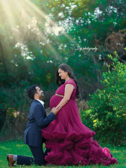 A tender moment with the father-to-be kneeling to kiss the baby bump. The mother-to-be is wearing a wine-colored ruffled gown.