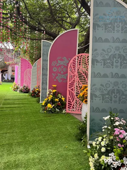 A playful and colorful entrance pathway for a Mayra ceremony, lined with custom-printed arches in shades of pink and green.