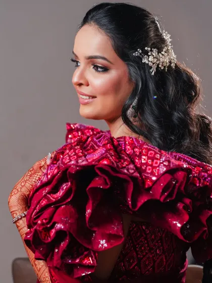 A close-up profile shot of the bride, highlighting her elegant hairstyle with a pearl accessory and the unique ruffled design of her blouse.