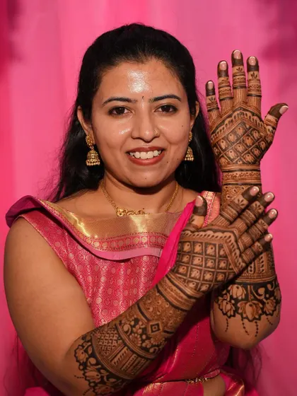 A happy bride in a pink saree, proudly displaying her full-arm grid-patterned mehendi.