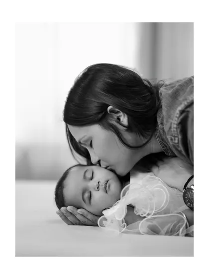 A mother's gentle kiss on her sleeping baby's forehead. This black and white close-up is a timeless expression of maternal love and tenderness.
