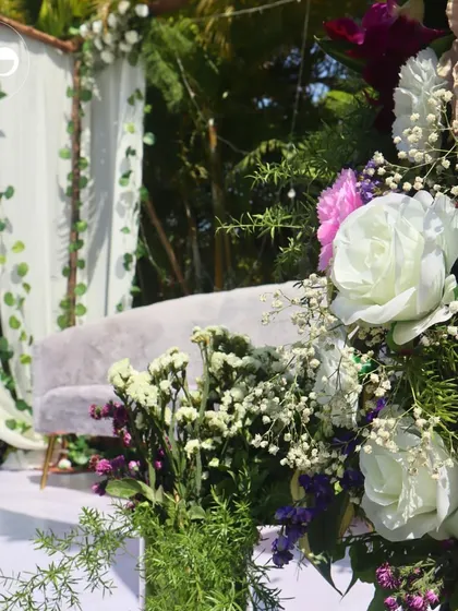 A close-up of the floral decor for an outdoor Roka. The arrangement of white roses, pink carnations, and greenery perfectly complements the natural, sunlit setting.