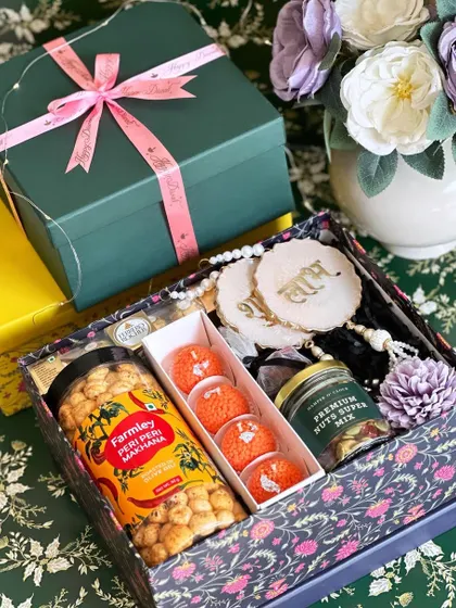 A printed blue Diwali box filled with peri-peri makhana, Ferrero Rocher, ladoo candles, and Shubh Labh resin wall hangings.