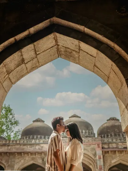 Framing the couple within a stone archway, with the domes of a historic monument visible in the background. This is a classic pre-wedding shot that combines romance with architectural beauty.