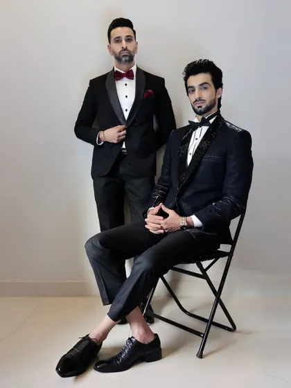 A full-length portrait of our designers, showcasing two distinct tuxedo styles. One is a classic black tuxedo with a satin lapel, while the other is a modern, textured design, reflecting our diverse range.