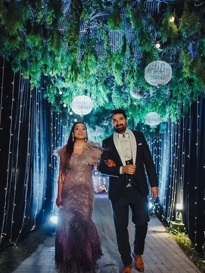 The couple makes a stylish entrance through a tunnel of lights, with a ceiling of hanging greenery and disco balls.