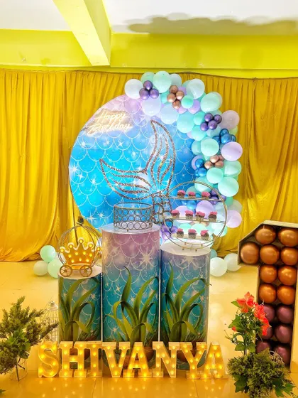 An enchanting mermaid themed birthday decoration. The setup features a sparkling mermaid tail backdrop, under-the-sea themed pedestals, and the birthday girl's name in marquee letters.