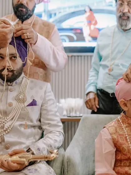 The Sehra Bandi ceremony, where the groom's turban is tied, with a young family member looking on. I capture the passing of traditions between generations.
