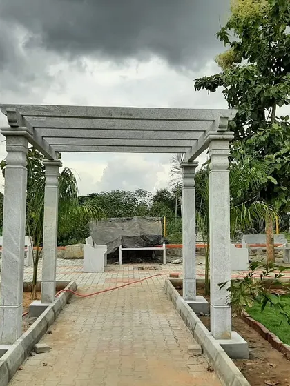 A finished stone pergola installed at the end of a paved walkway. This structure adds height and architectural interest to the garden landscape.