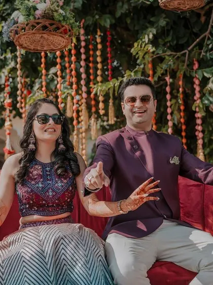 Mehendi goals! The couple sits together on a vibrant red couch, showing off their henna and their fun-loving attitudes during their destination wedding celebration.