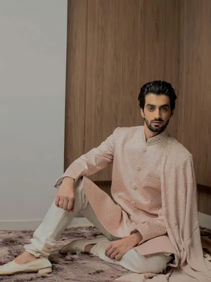 A relaxed pose in our rose gold sherwani, highlighting the intricate tonal embroidery that flows across the garment. It's a piece designed for both grandeur and comfort.