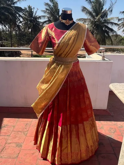 A red and gold traditional half saree with a tissue dupatta.