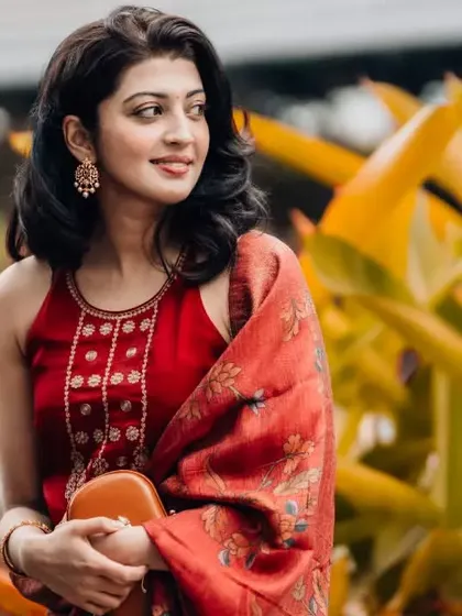 A beautiful portrait of actress Pranitha Subhash against a backdrop of lush yellow-green foliage. The natural lighting and her warm expression create a soft and inviting image.