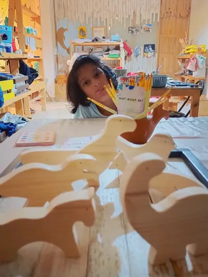 A child peeking over a collection of wooden dinosaurs, ready for a painting session. Our kits are designed to spark imagination and provide hours of creative fun.