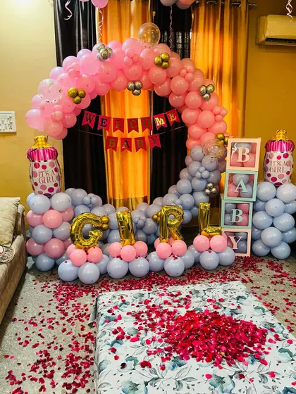 Here you can see the welcome home decoration set up in a bedroom. The bed is covered with rose petals, and the balloon arch with "GIRL" foils creates a festive atmosphere for the new mother and baby.