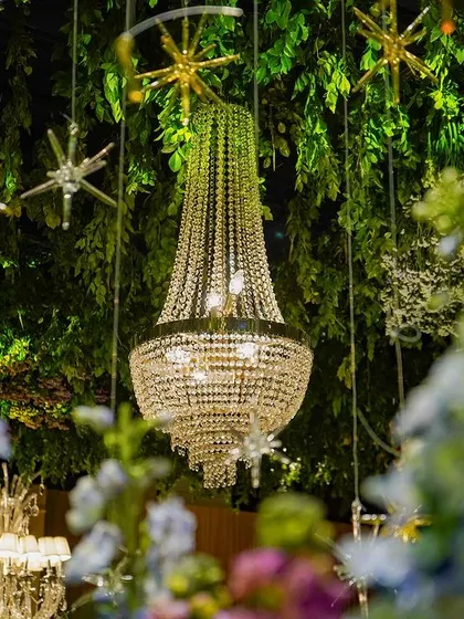 A crystal chandelier hangs amidst a ceiling of lush greenery and golden stars. This shot perfectly captures the theme's blend of natural beauty and sparkling elegance.