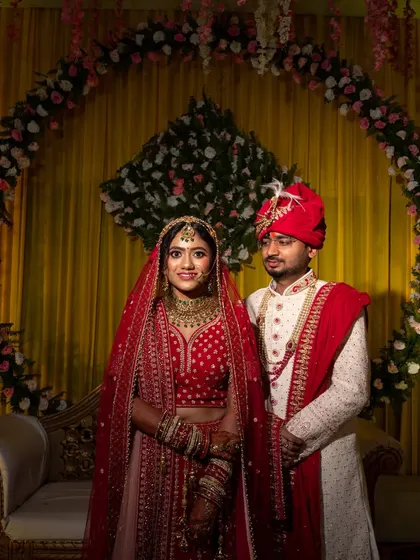 A classic wedding portrait of the couple on their stage, against a backdrop of yellow curtains and floral decor.