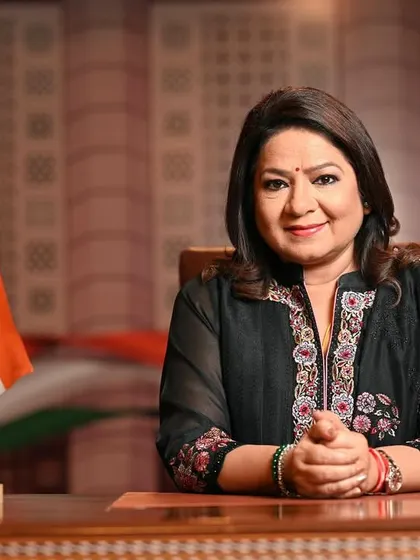 A formal desk portrait of Mrs. Anuradha Prasad with the Indian flag. This setup adds a sense of national pride and official stature to her corporate branding.