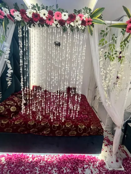 A full view of the bed with its floral canopy, hanging flower strings, and petal-strewn floor, ready for the newlywed couple.