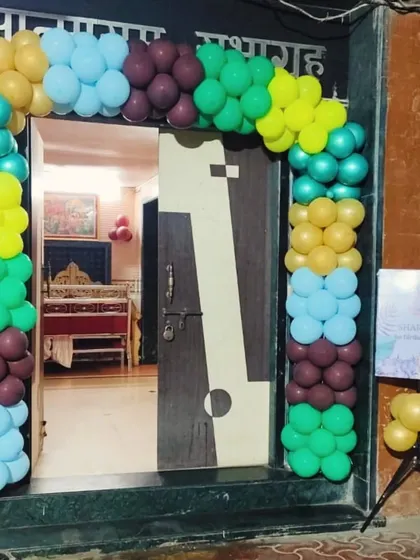 This balloon arch uses a distinct color palette of teal, yellow, blue, and maroon to frame a doorway. A small welcome easel stands beside it, making it a complete and inviting entrance setup for a baby party.