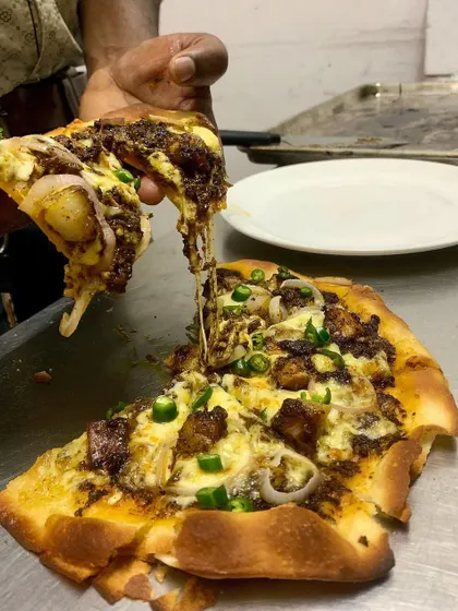 A creative twist on a classic, our Pandi Curry Pizza. This slice shows the incredible cheese pull, with our slow-cooked peppery pork, fresh mozzarella, and onions on a thin, crispy crust.