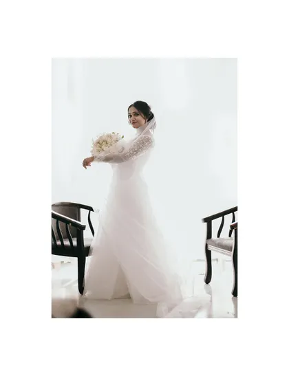 A full-length portrait of the Christian bride in her flowing white gown, holding a bouquet of white roses, the picture of elegance.
