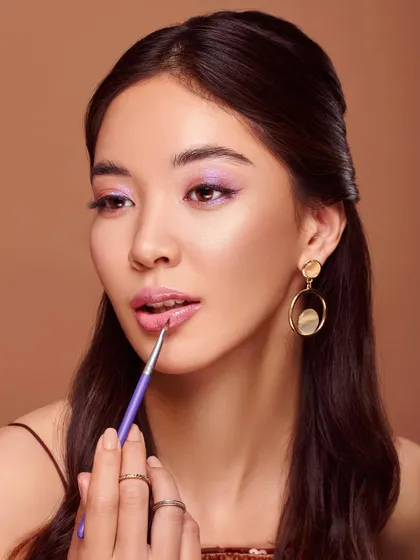 This image focuses on the application of lipstick with a brush, emphasizing precision and a flawless finish. The model's pose is elegant, and the overall look is polished and sophisticated, making the brush appear as an essential tool for a perfect pout.