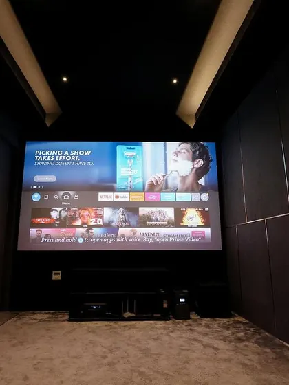 The front of the room, with the AV equipment neatly arranged below the screen. The dark walls and ceiling ensure a high-contrast, cinematic image.