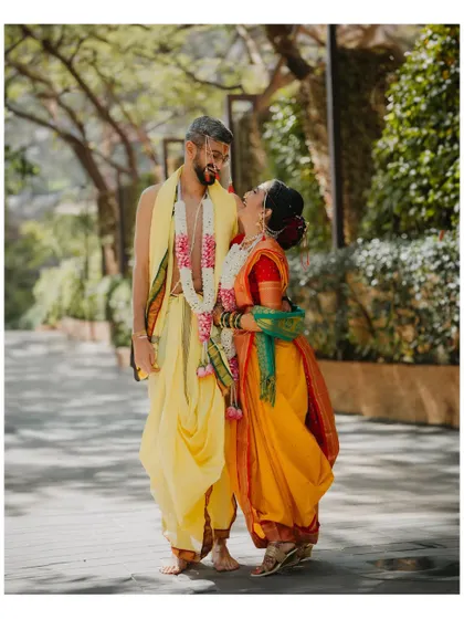 A candid, happy moment between the bride and groom in their traditional yellow wedding attire. The bride is looking up at the groom with a wide, joyful smile.