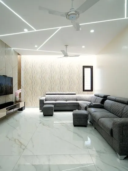 This living room design for a villa features dramatic geometric ceiling lights, a textured accent wall, and a comfortable quilted sectional sofa, all contributing to a modern and sophisticated ambiance.