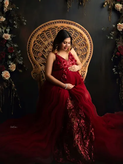 A truly enchanting portrait. This mom-to-be is seated on the peacock chair in a deep red gown, surrounded by a dark, romantic floral setup.