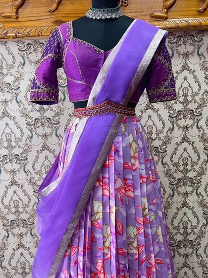 A trendy lavender floral half saree. The pleated skirt is paired with a handcrafted maggam work blouse and a pure organza dupatta for a fresh, contemporary look.