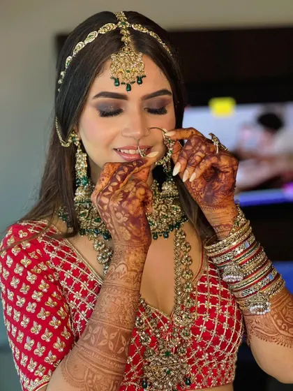 The final touches make all the difference. Here, the bride is adjusting her nath, showcasing the complete look with her smokey eyes, intricate mehendi, and stunning green jewelry.