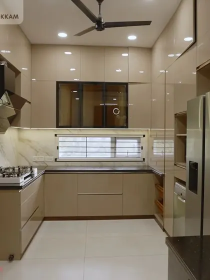 A look at a U-shaped modular kitchen from an individual villa in Ayappakkam. The beige high-gloss cabinets create a warm and inviting atmosphere, paired with a black granite countertop and integrated appliances for a seamless and modern look.