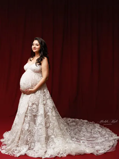The long, intricate lace train of this white gown is showcased against a dramatic red backdrop, creating a stunning contrast.