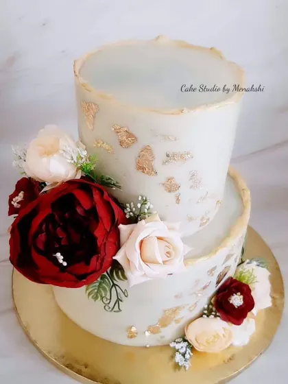 A beautiful two-tier floral cake with a textured, gold-leaf finish. This no-fondant design is adorned with a mix of deep red and soft pink flowers, creating a rich and romantic look.