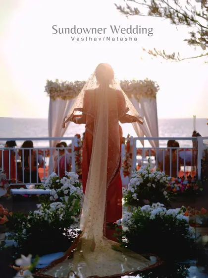 A "sundowner" bridal portrait. The bride is silhouetted against the setting sun and the wedding mandap, her veil catching the golden light in a truly magical and atmospheric shot.