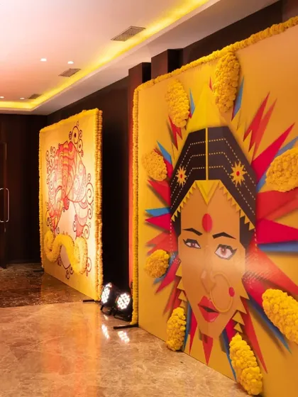 Large, artistic graphic panels featuring traditional Indian motifs and figures, framed with marigold garlands, create a unique and modern entrance gallery.