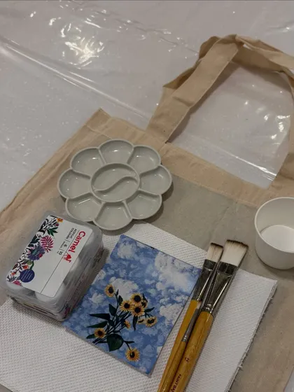The supplies for our tote bag painting workshop, including a reference image, paints, brushes, and of course, the tote bag.