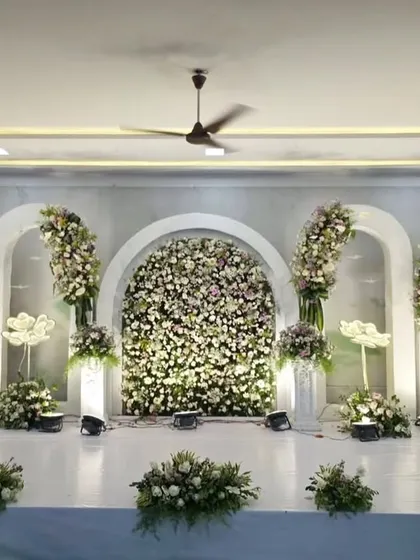 A pristine all-white reception stage. The backdrop of white arches is filled with a dense wall of white flowers, creating a breathtakingly elegant and sophisticated look.